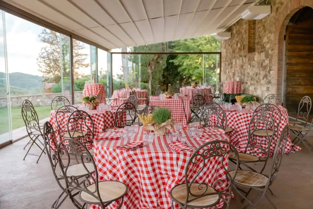 Round tables set with red and white checkered tablecloth, iron chairs with wooden seats. Aromatic herbs, spaghetti and can of tomato as centerpiece for decorating in true Italian style
