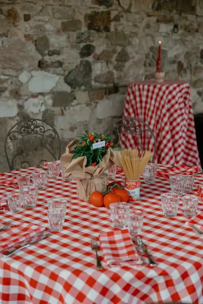 Round tables set with red and white checkered tablecloth, iron chairs with wooden seats. Aromatic herbs, spaghetti and can of tomato as centerpiece for decorating in true Italian style